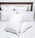 A neatly made bed with a dark wood and beige upholstered headboard is topped with six white hotel pillows. In front, two Keeco Choice Hotels® Soft and Firm Polyester Pillows, each featuring colorful fabric tags, rest on a white quilted comforter.