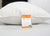 A white, silky-smooth hypoallergenic Best Western® Dreammaker Pillow by Keeco rests on a bed with a white sheet. An orange and white “Silky Soft Fiber” label stands upright against the pillow, displaying product details.