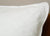 Close-up of the Down Etc. Diamond Support Feather & Down Pillow | Medium-Firm, featuring its white quilted diamond-pattern cover on a brown wooden surface, with a light-colored wall in the background. Brand: Down Etc.