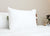 A large, white Sysco Guest Supply Dream Escape Down Alternative Pillow (formerly Dream Essence) sits upright on a neatly made bed, while a plant on a wooden bedside table enhances the minimal, hypoallergenic appeal.