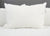A large, fluffy white Pillowtex Triple Core Lyocell Pillow | Medium Support by Pillowtex sits upright on a white bed with a quilted comforter and gray upholstered headboard, offering great neck support and featuring a small tag on the edge.