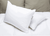 Two Blue Label Firm Pillows by Keeco, featured at many Choice® Hotel brands, with smooth pillowcases rest on a white mattress cover; behind them are two beige pillows upright against the headboard. One firm pillow slightly overlaps the other.
