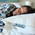 A woman with dark hair, in a floral top, sleeps peacefully on a Keeco Choice Hotels® Soft and Firm Polyester Pillow Combo Pack (2 pillows); the care tag is visible, and a softly blurred background enhances her restful scene.