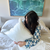 A woman with long dark hair sits on a bed with white bedding, hugging a Keeco Choice Hotels® Soft and Firm Polyester Pillow Combo Pack (Includes 2 Pillows); behind her is a large abstract blue and green painting.